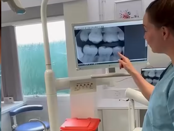 Dentist reviews dental X-rays on a monitor with a patient in a clinic.