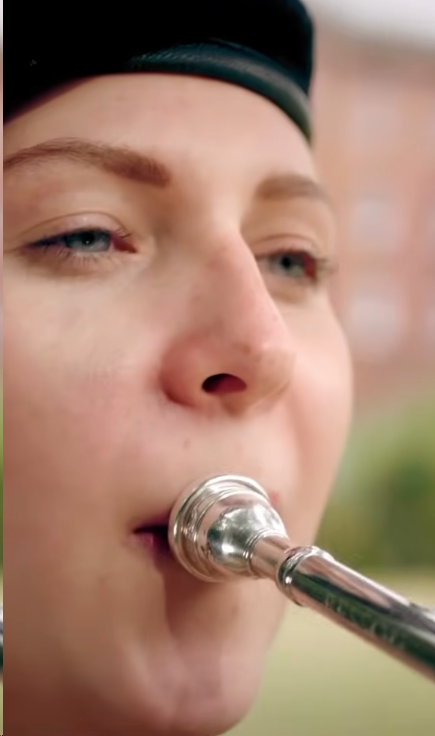 A person wearing a black hat is playing a silver trumpet outdoors.