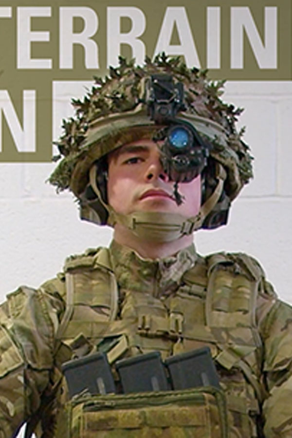 A soldier wearing camouflage gear and a helmet with goggles stands in front of a sign partially reading "TERRAIN."