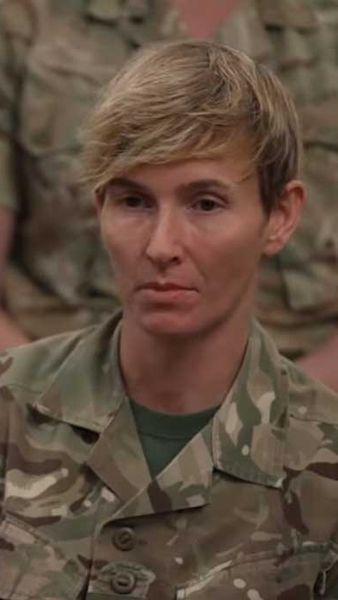 Female soldier in uniform sitting down with other soldiers.