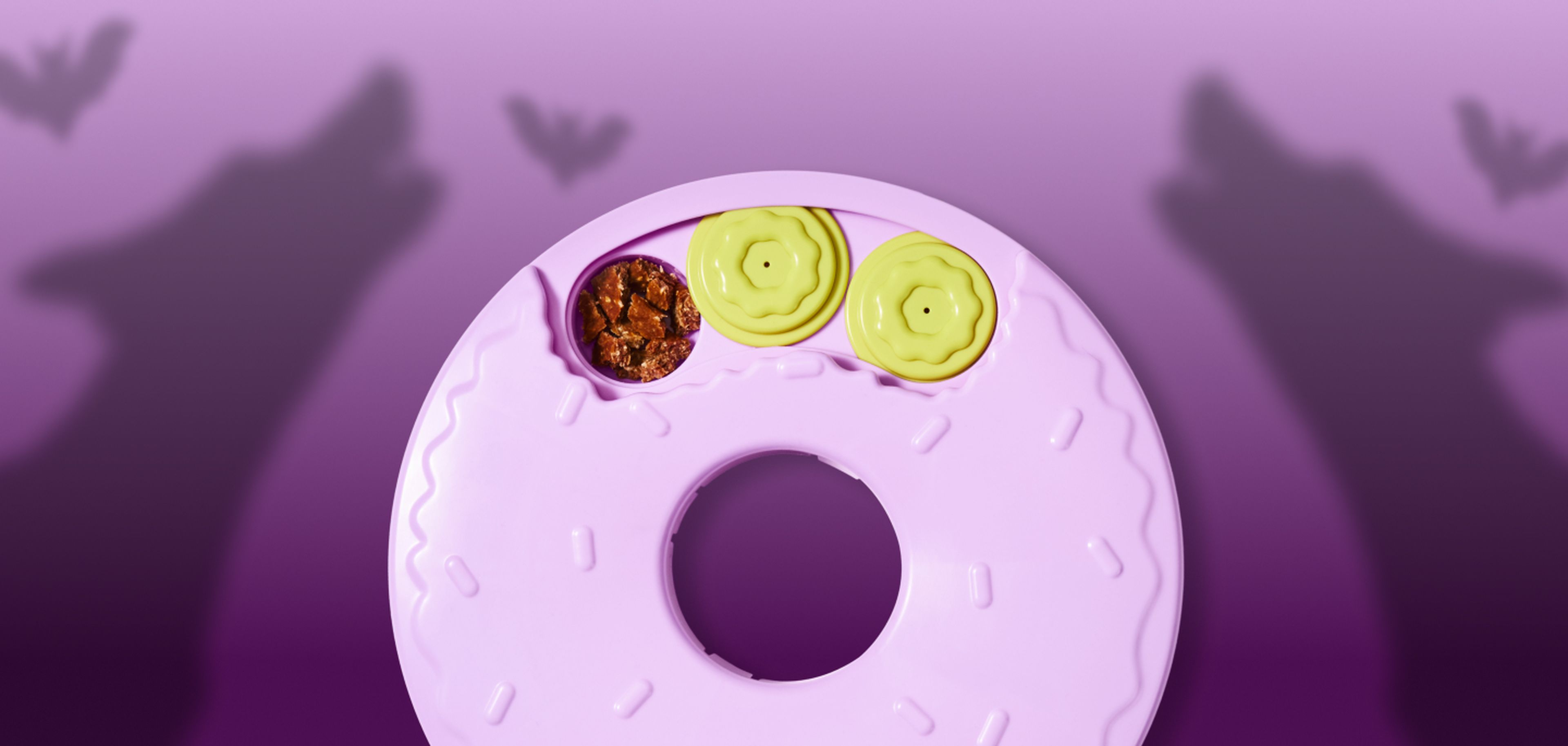 A pink donut-shaped object with sprinkles, a chocolate filling, and two yellow circles on top, set against a purple background with shadow puppets.