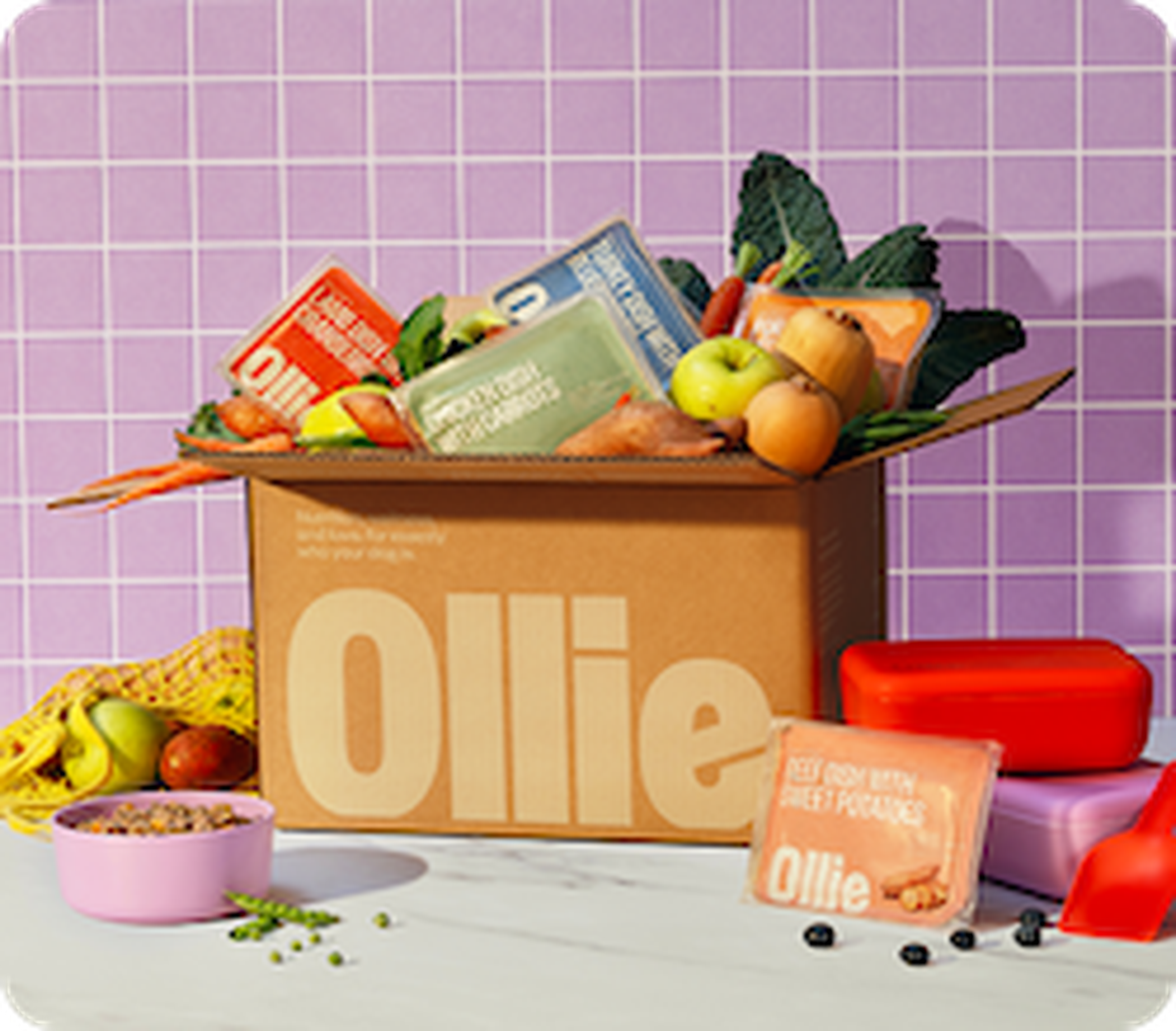 Box labeled "Ollie" filled with packaged food, vegetables, and fruits, set on a table with a purple tile background.
