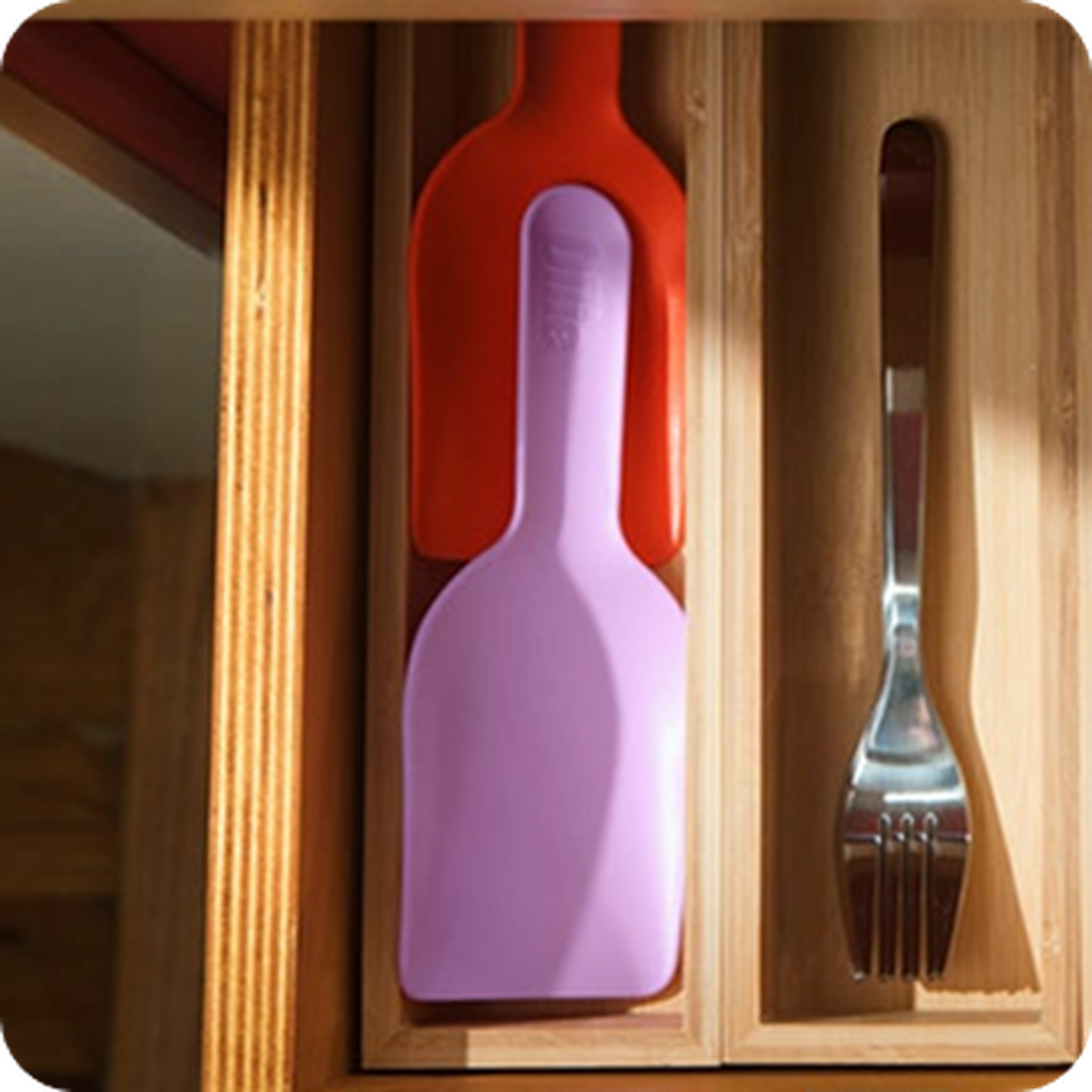 Wooden drawer with two colorful spatulas in red and pink on the left, and a stainless steel fork on the right.