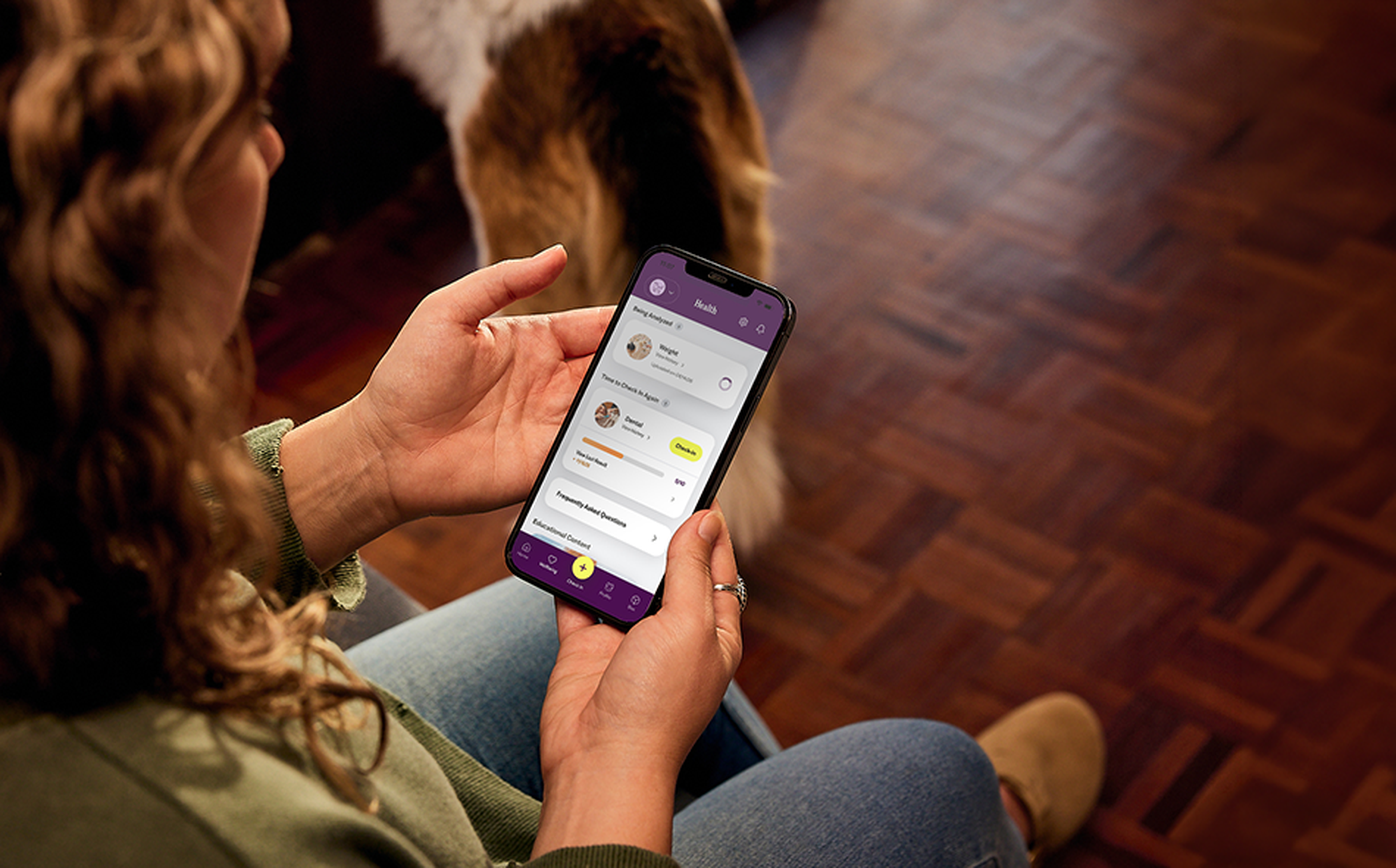 A person using a smartphone app with a purple interface while sitting on a wooden floor, with a dog nearby.
