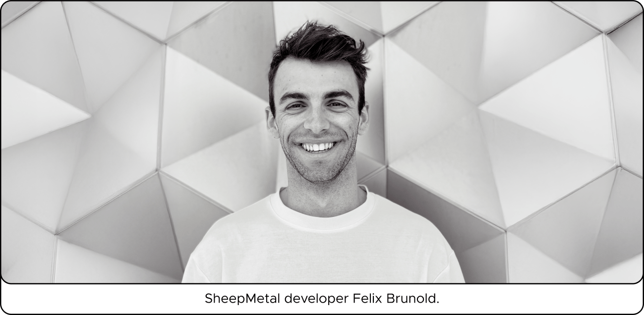 Smiling person in a white shirt stands against a geometric, textured wall.
