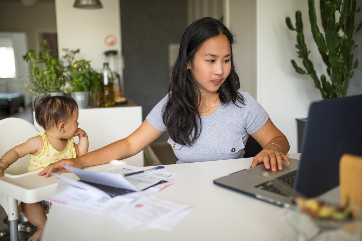 A woman on the laptop at home, whilst looking after a child