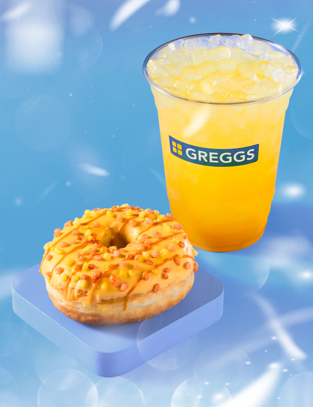 A vibrant mango drink and mango doughnut on a light blue background with gentle rainbow refractions scattered across