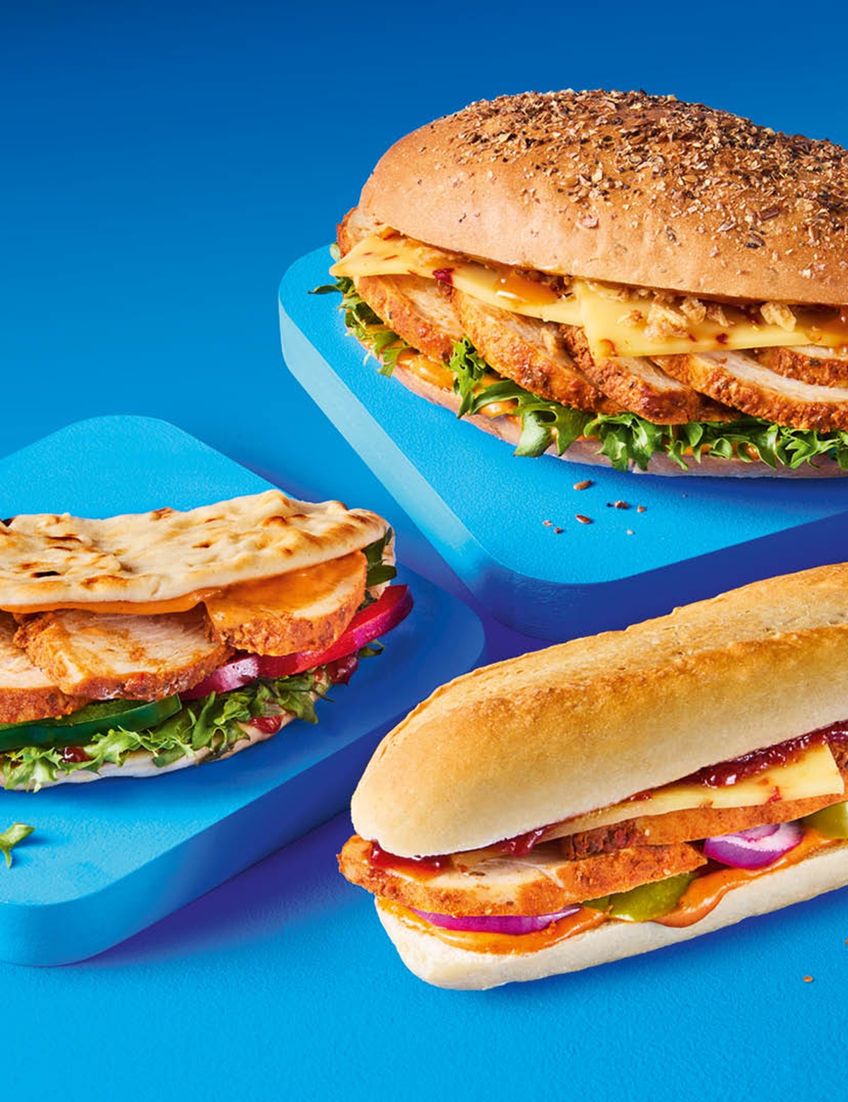 Three sandwiches on a blue surface: a flatbread, an oval bite and a baguette
