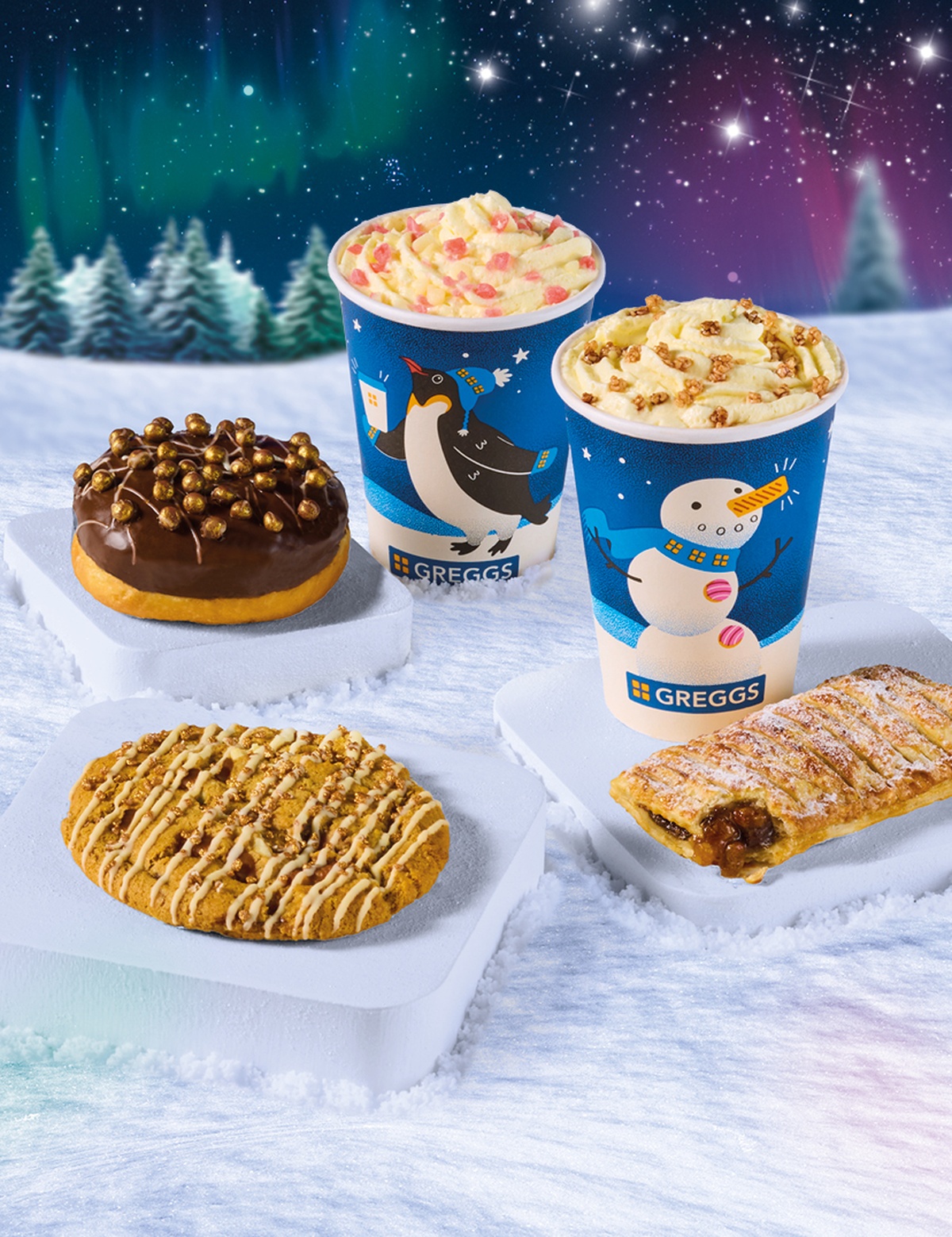 Assorted Greggs treats, including a donut, cookie, Sweet Mince Pie Roll, and festive-themed hot drinks, displayed on snow with a snowy forest and aurora in the background.