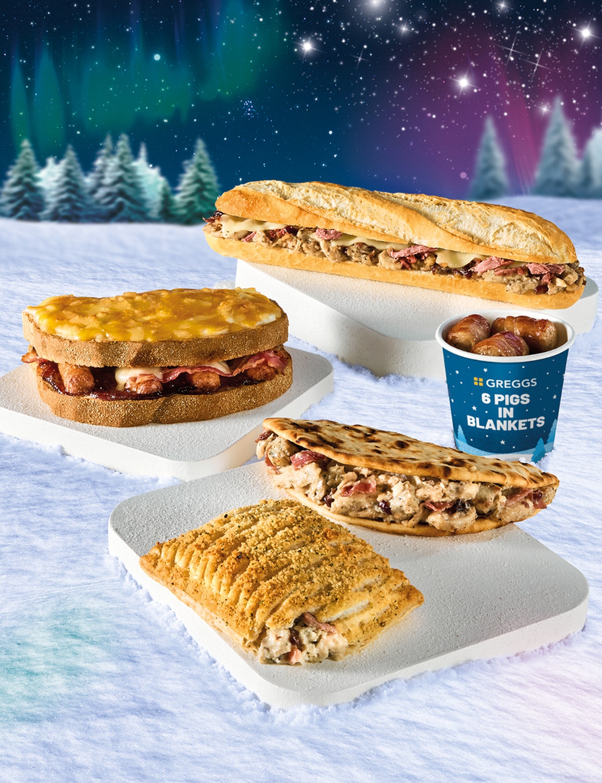 Assortment of festive sandwiches and savoury items on snowy terrain with trees and Northern Lights in the background.