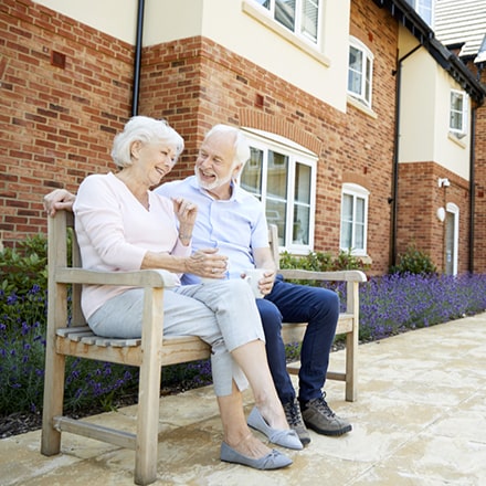 Elder couple on a wooden bench, laughing with their arms around each other