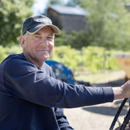 A male farmer wearing a Welch's cap, driving a tractor