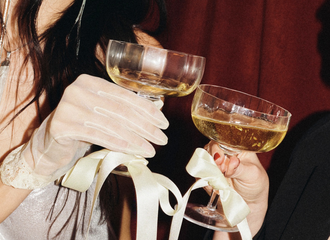 A group of people reaching for oysters on ice, a large baguette, red grapes, and wine glasses on a dining table.