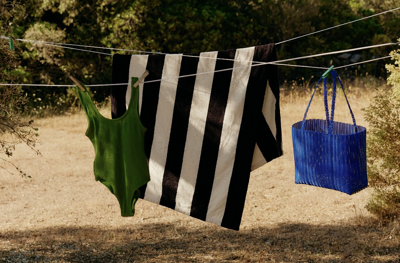 A green swimsuit, a black and white striped towel, and a blue bag hanging on a clothesline outdoors.