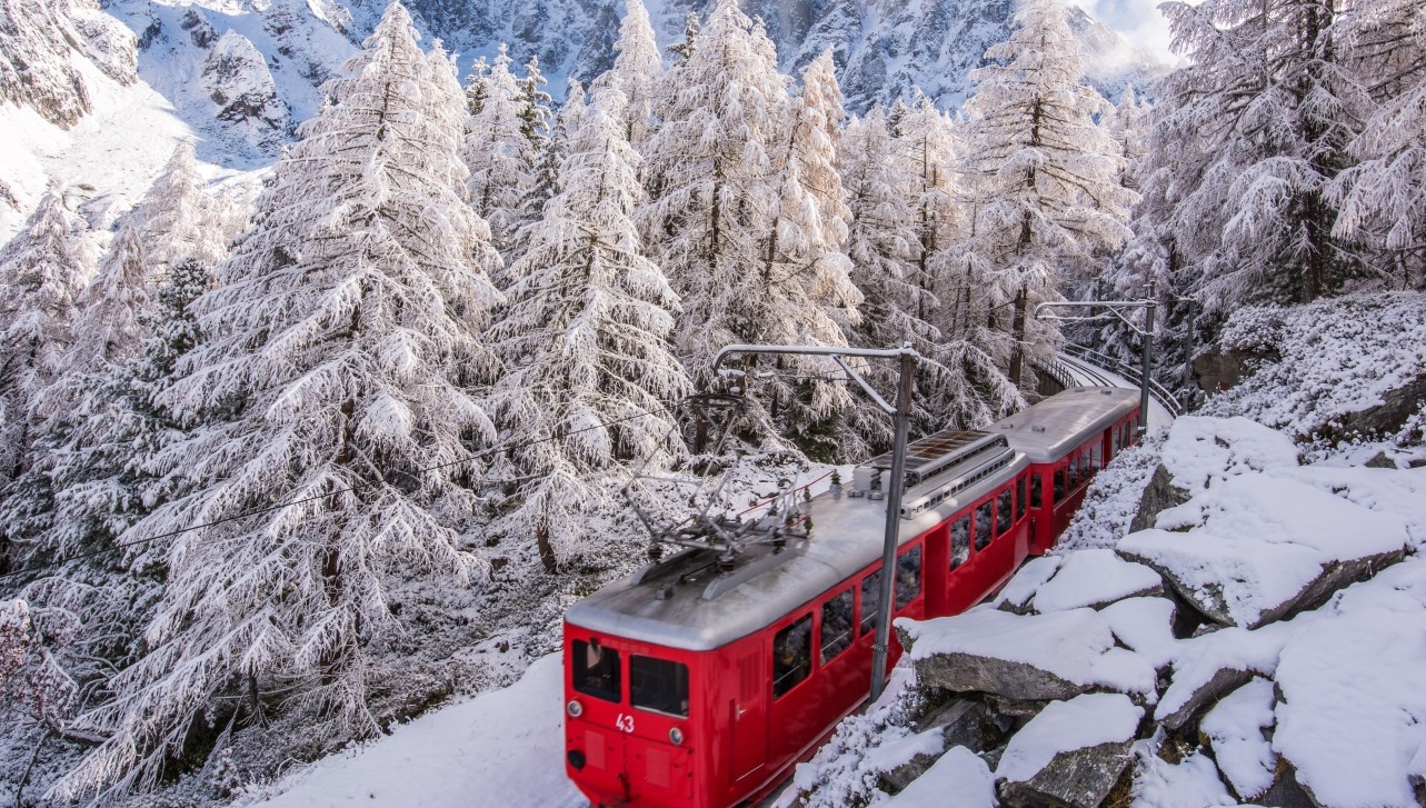 A red train travels through a snow-covered landscape, with the Matterhorn mountain visible in the background under a clear blue sky.