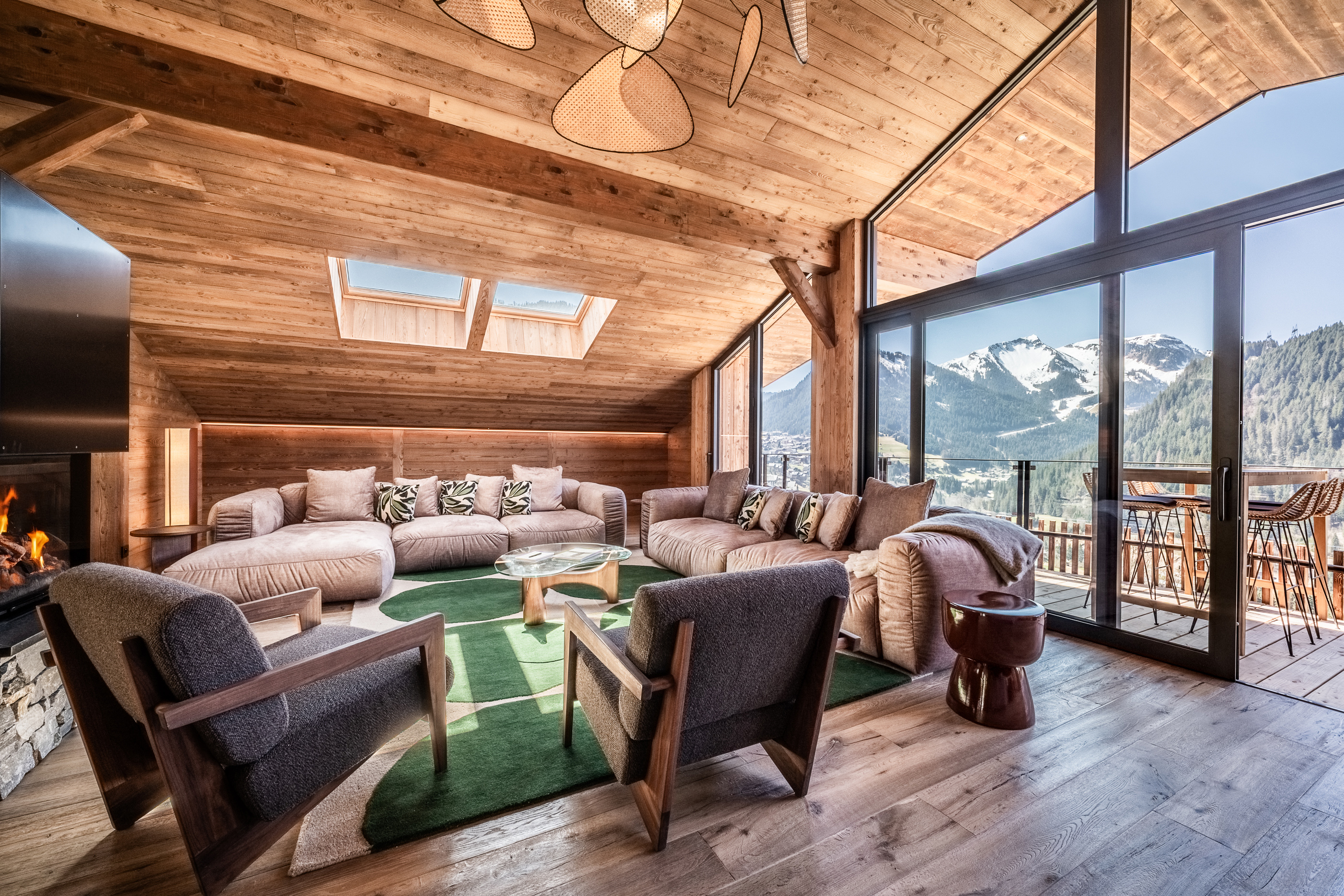 Cozy mountain chalet living room with wooden interior, large windows, plush sofas, armchairs, and a view of snow-capped peaks.