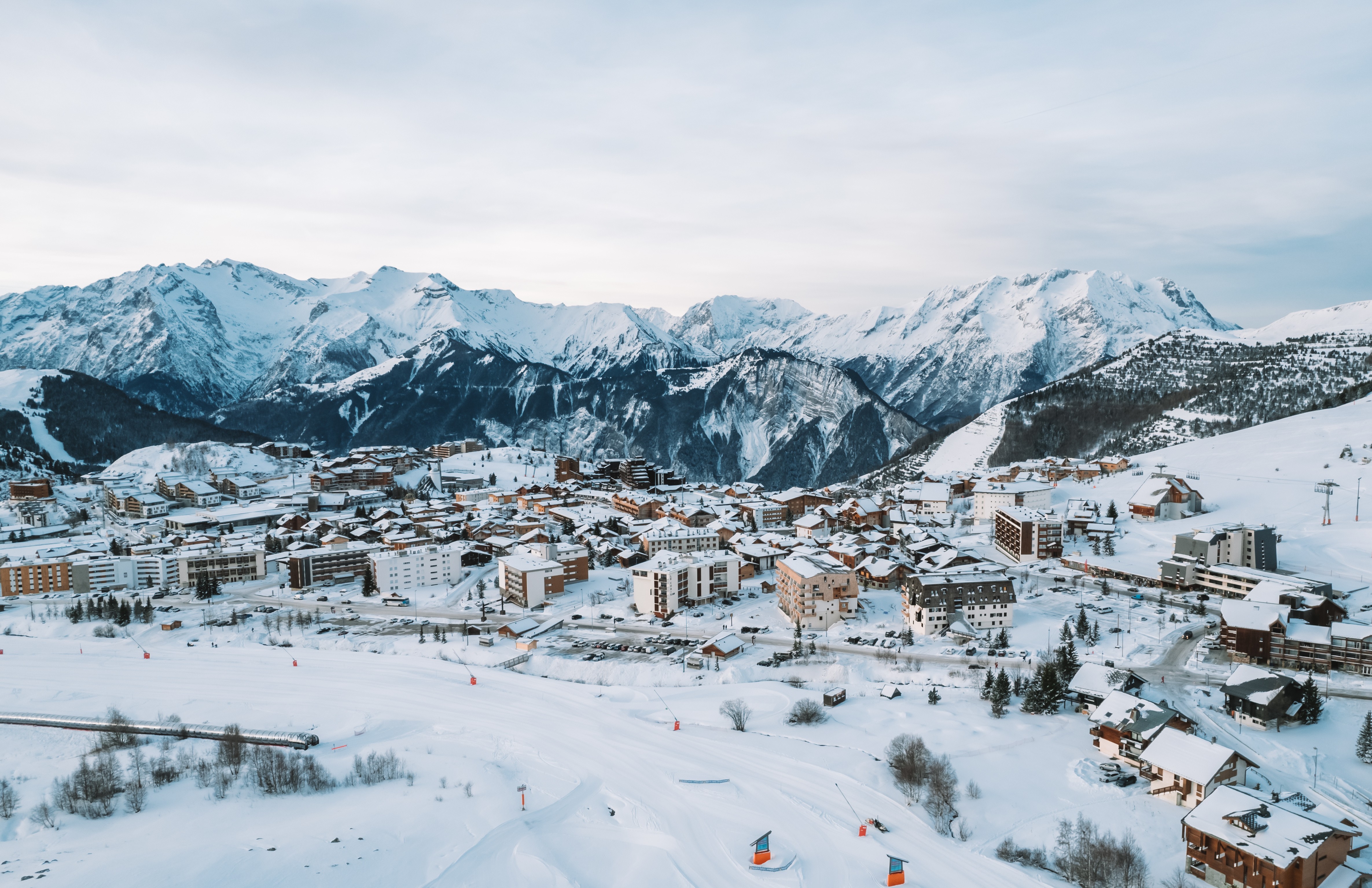 Mountain view from a wooden balcony, overlooking snowy peaks and a skier below under a cloudy sky.
