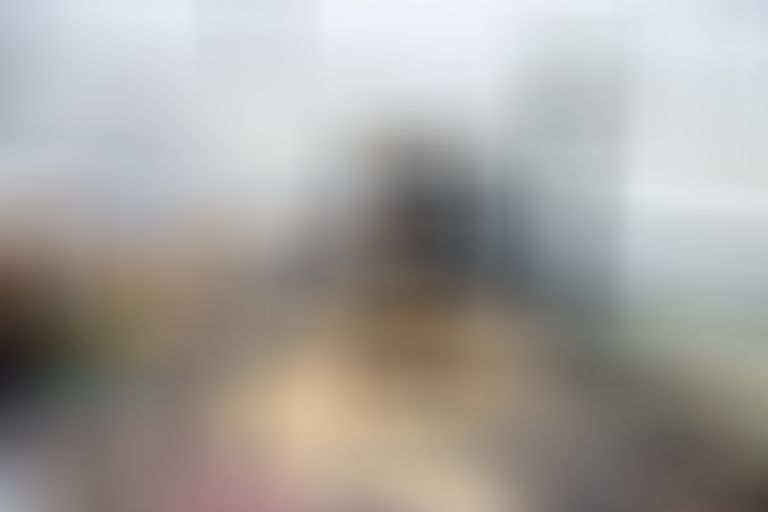 A conservator examines a large painting with a microscope, surrounded by brushes and tools on a table in an art restoration studio.