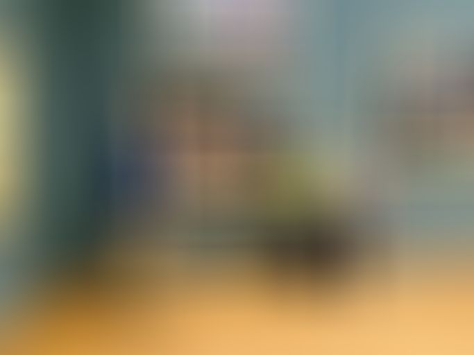 Three people stand in an art gallery, posing in front of a large framed painting. The room has wooden floors and blue-green walls.