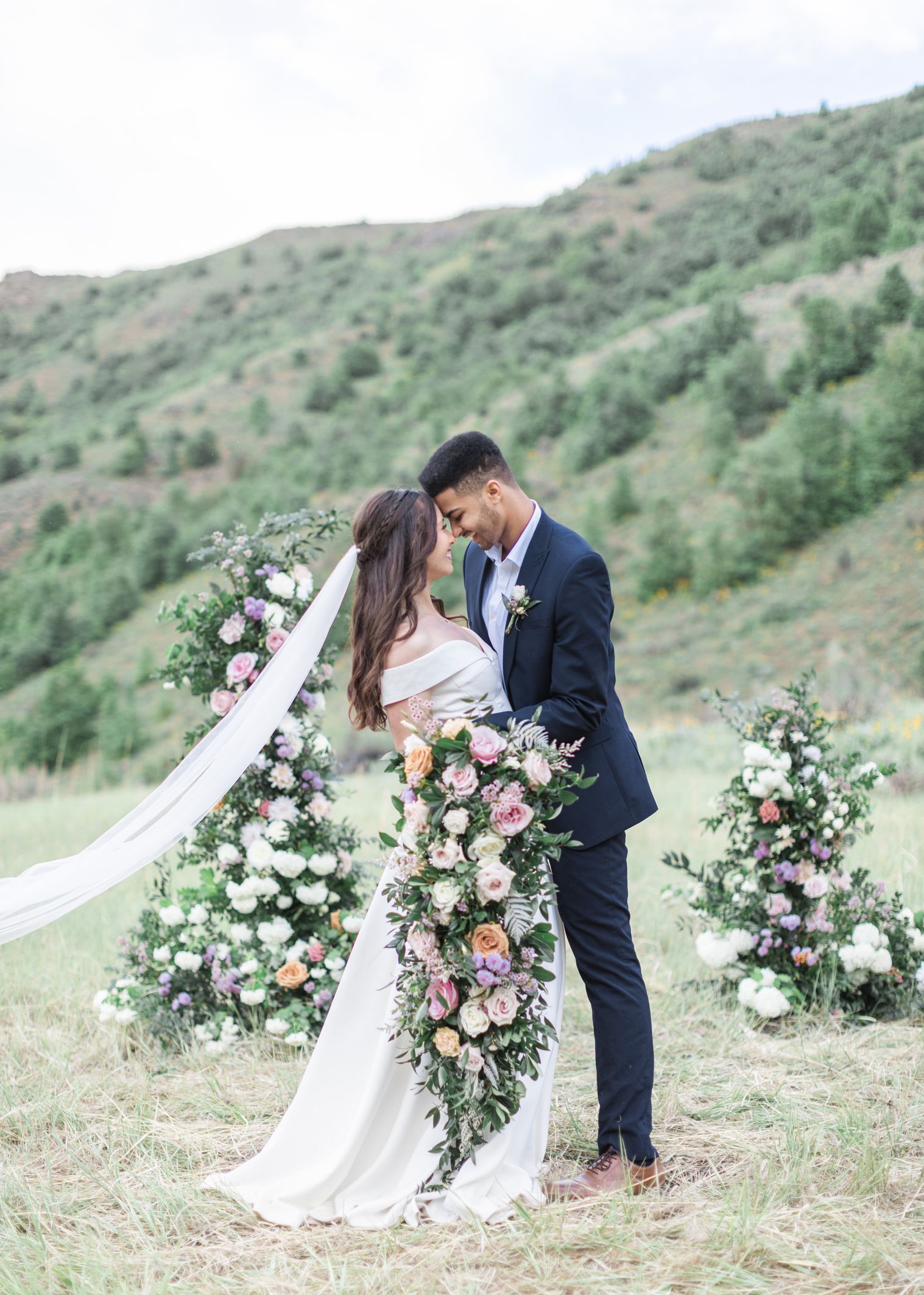 Couple holding a Bronte's Florals cascading bouquet, sharing a moment in the Utah mountainside greenery.