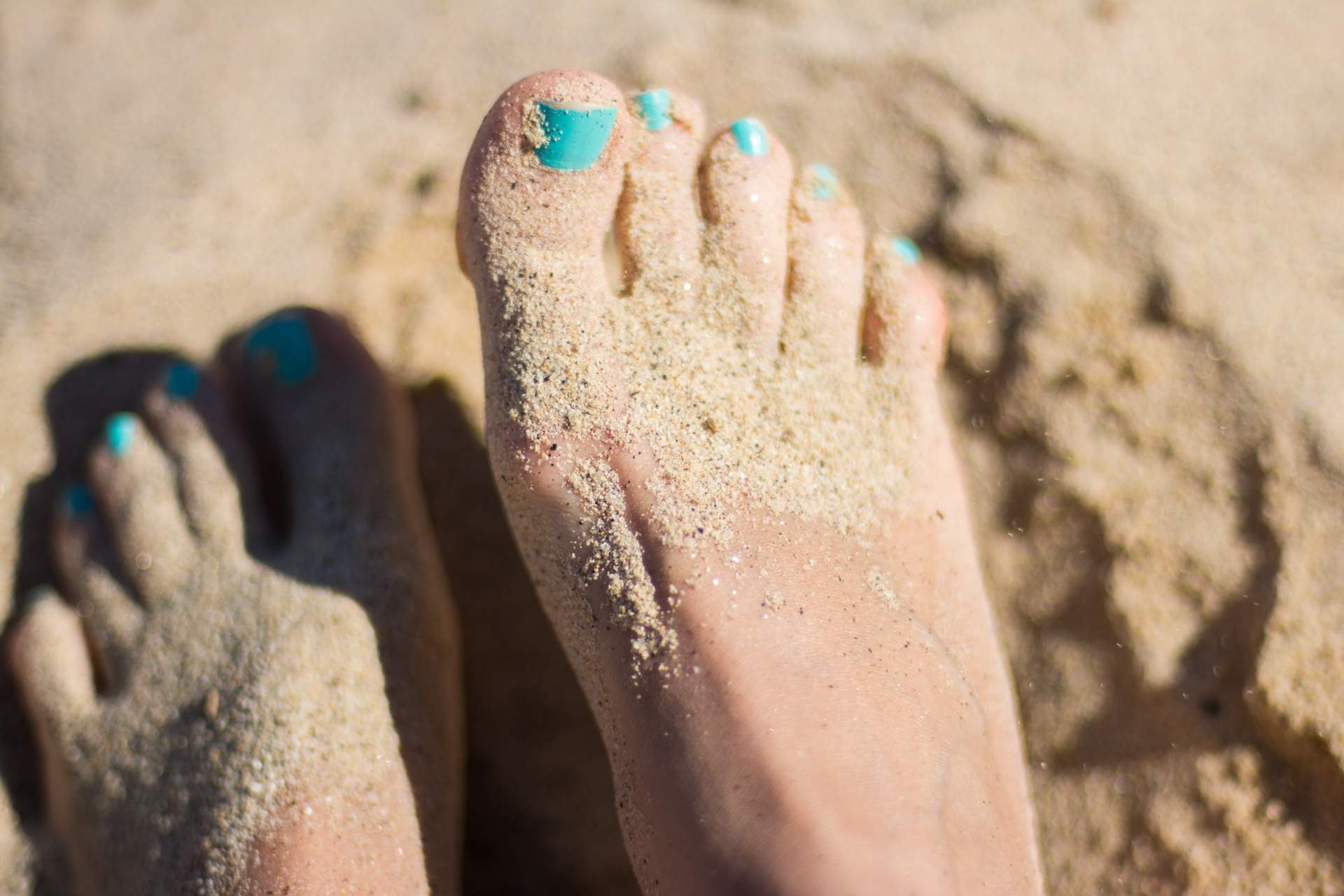 Feet and toes with nail polish in the sand