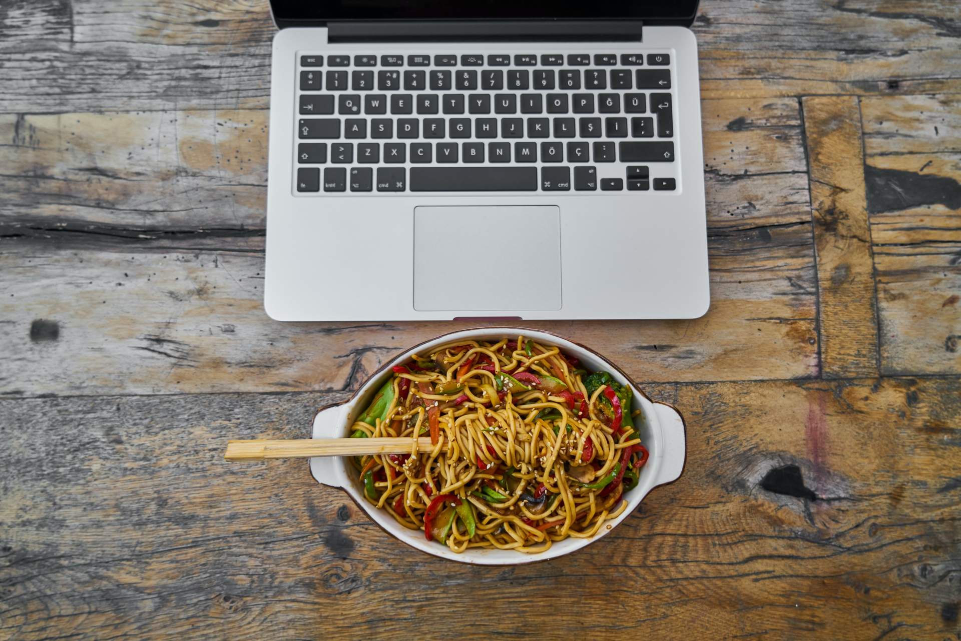 Dish of Asian noodles in front of a laptop
