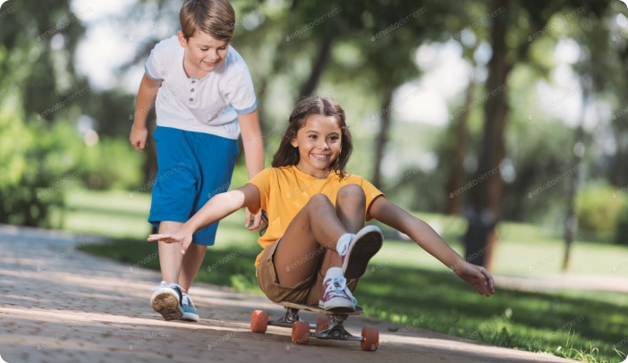 Boy pushing a girl sitting on a skateboard down the sidewalk. Kids are having fun!