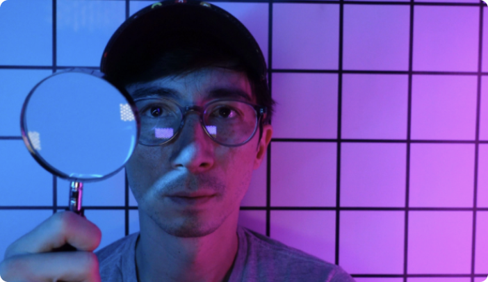 Man with baseball cap and glasses holding magnifying glass in front of his face