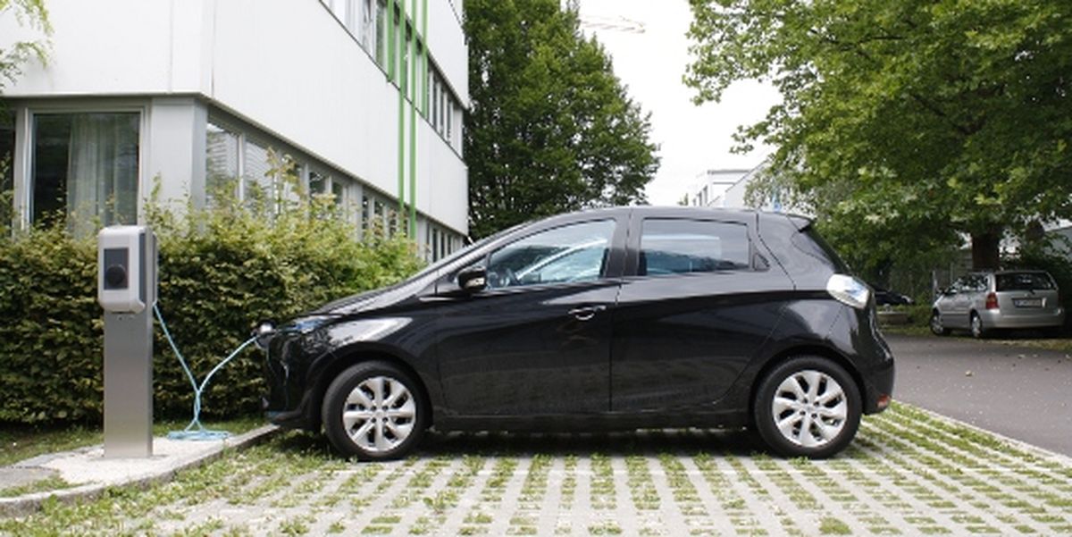 Auto elettrica nera collegata a una stazione di ricarica KEBA su un parcheggio erboso.