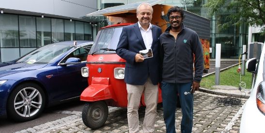 Deux hommes debout devant un rickshaw électrique rouge branché à une borne de recharge KEBA.