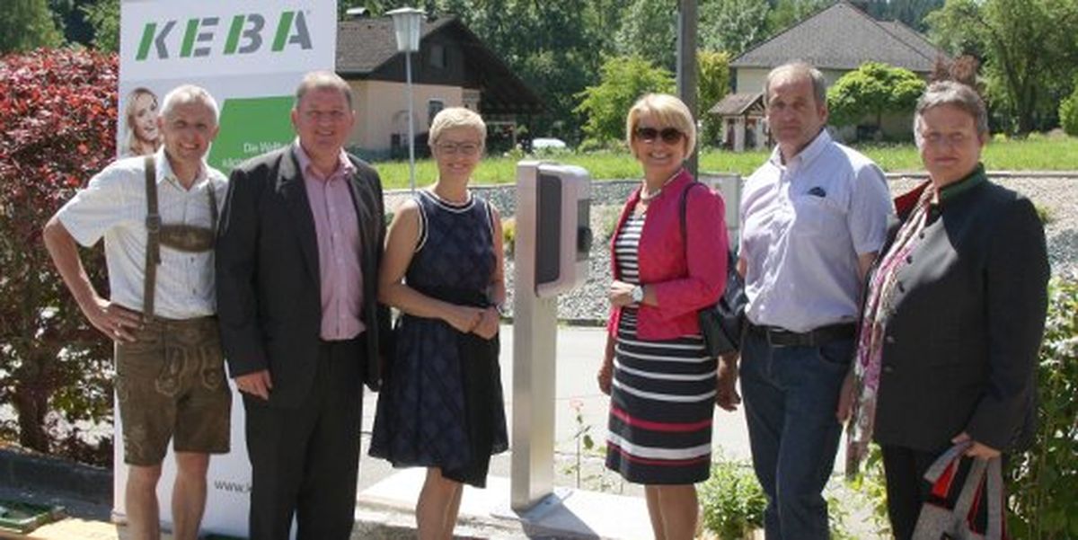 Group photo in front of a KEBA charging station with six people at an outdoor inauguration event.